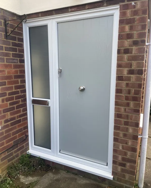 Solid light grey composite door with a centre knob, beside a white uPVC side panel with frosted glass and a letterplate.