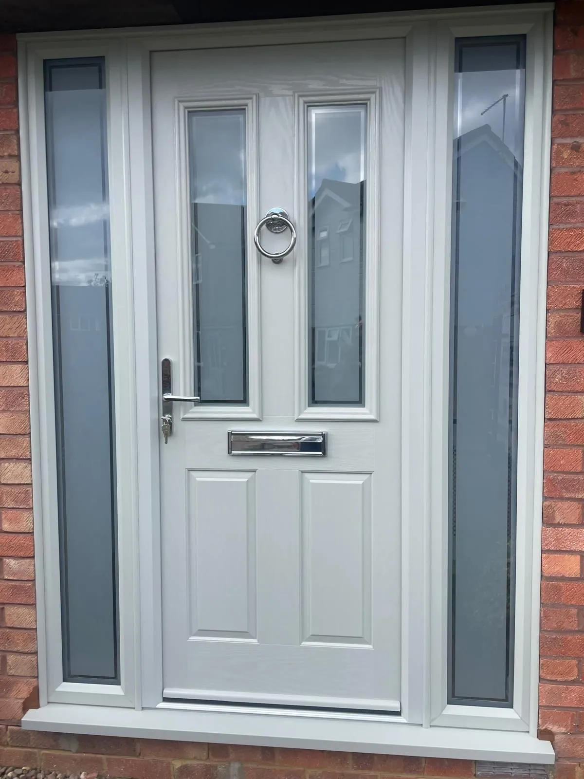Light grey composite front door with two glazed panels and a chrome ring knocker, flanked by full-height obscure glass side panels.