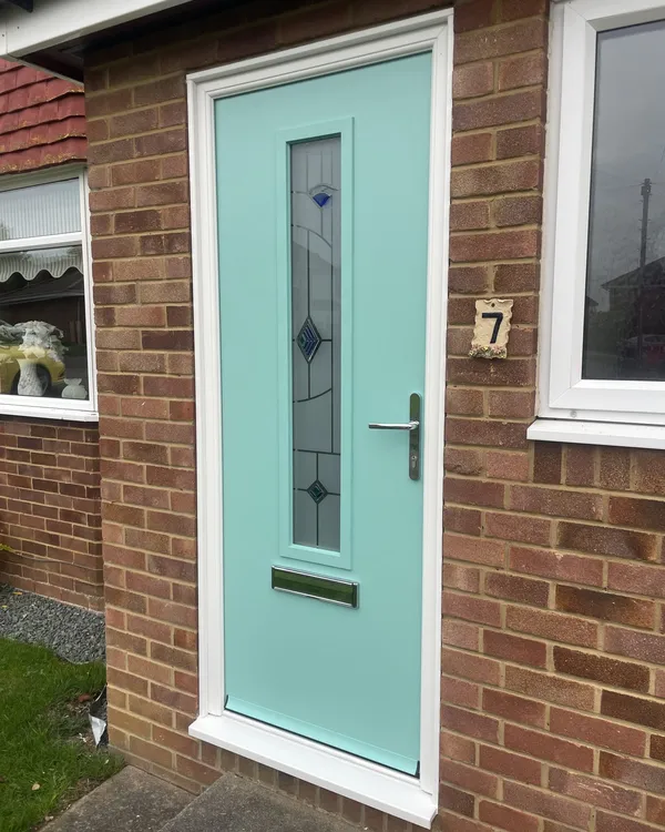 Mint green composite front door with a single tall decorative glass panel and chrome handle, in a white frame on a brick house.