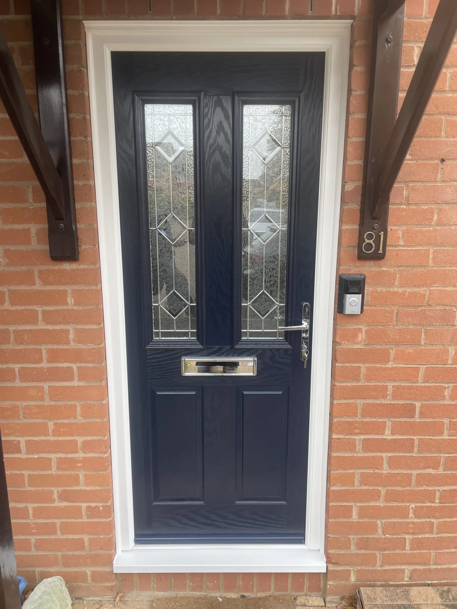 Navy blue composite front door with bevelled diamond glass panels and chrome furniture, in a white frame under a timber canopy.