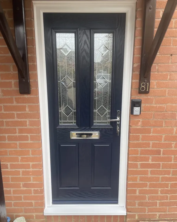 Navy blue composite front door with bevelled diamond glass panels and chrome furniture, in a white frame under a timber canopy.