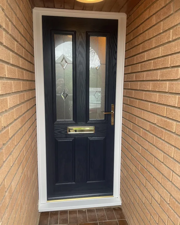 Navy blue composite front door with bevelled glass panels and brass furniture, fitted in a white frame inside a brick porch.