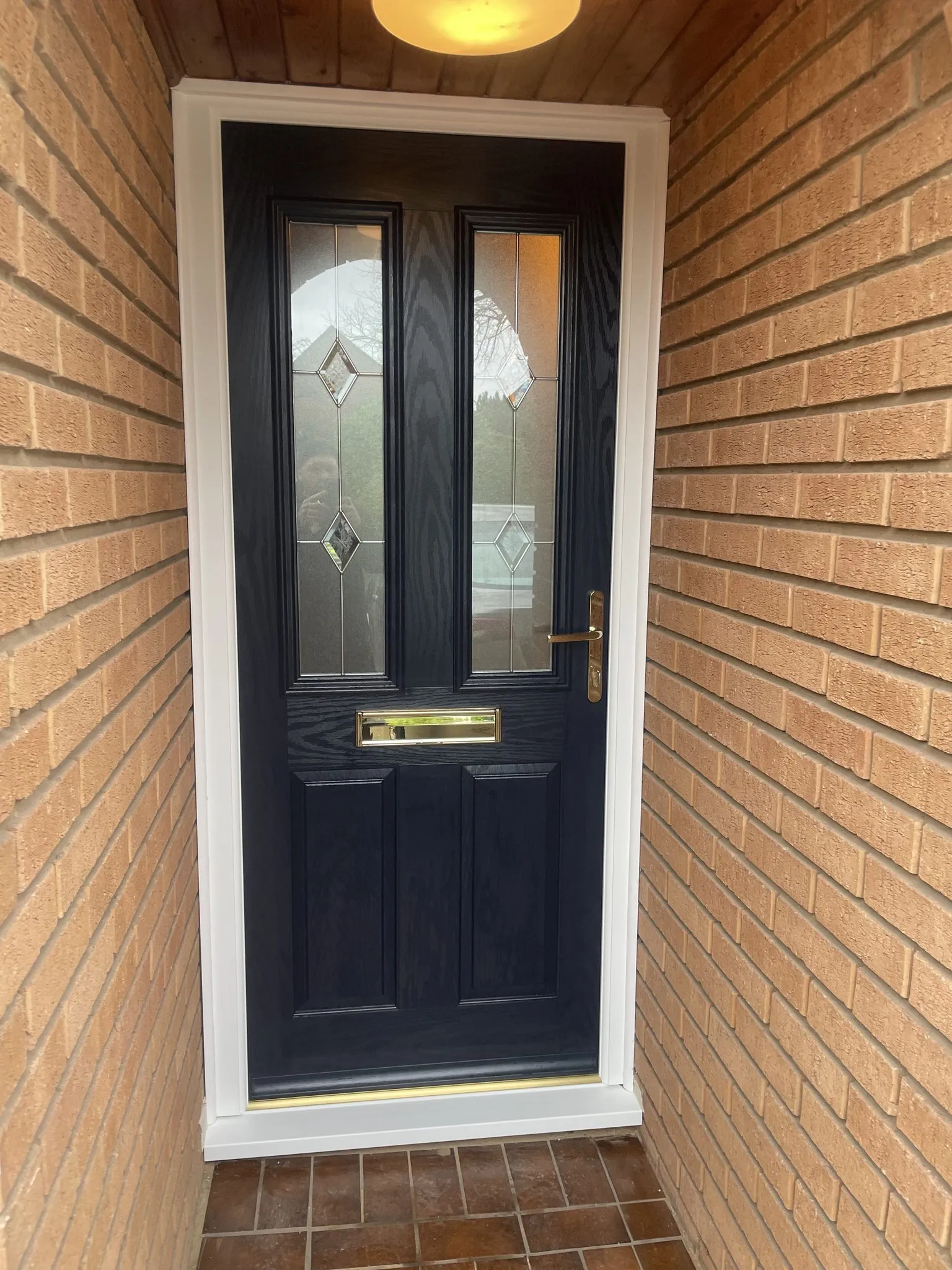 Navy blue composite front door with bevelled glass panels and brass furniture, fitted in a white frame inside a brick porch.