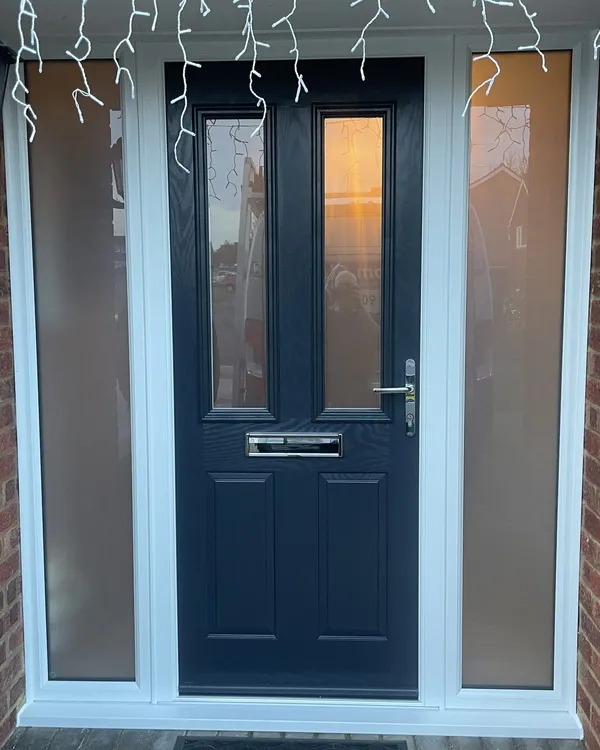 Navy blue composite front door with two glazed panels and chrome furniture, flanked by full-height frosted side panels in a brick porch.