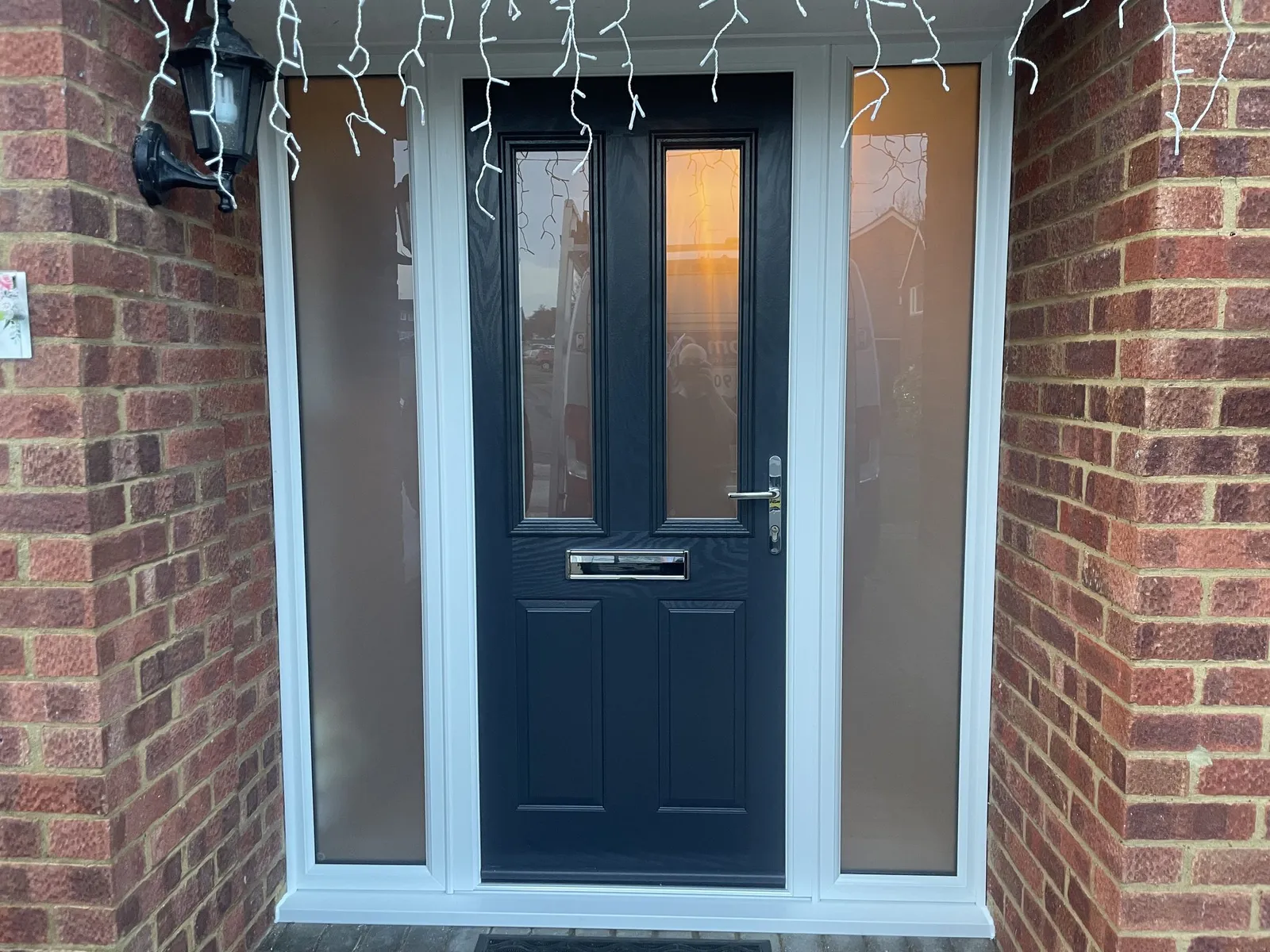 Navy blue composite front door with two glazed panels and chrome furniture, flanked by full-height frosted side panels in a brick porch.