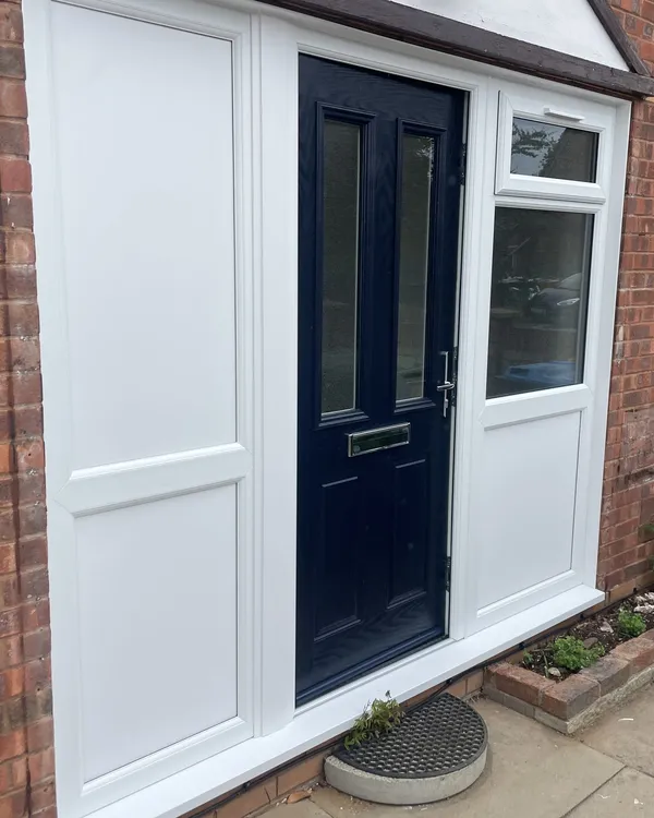 Navy blue composite door set into a white uPVC entrance screen with a solid side panel and a glazed window above a panel.