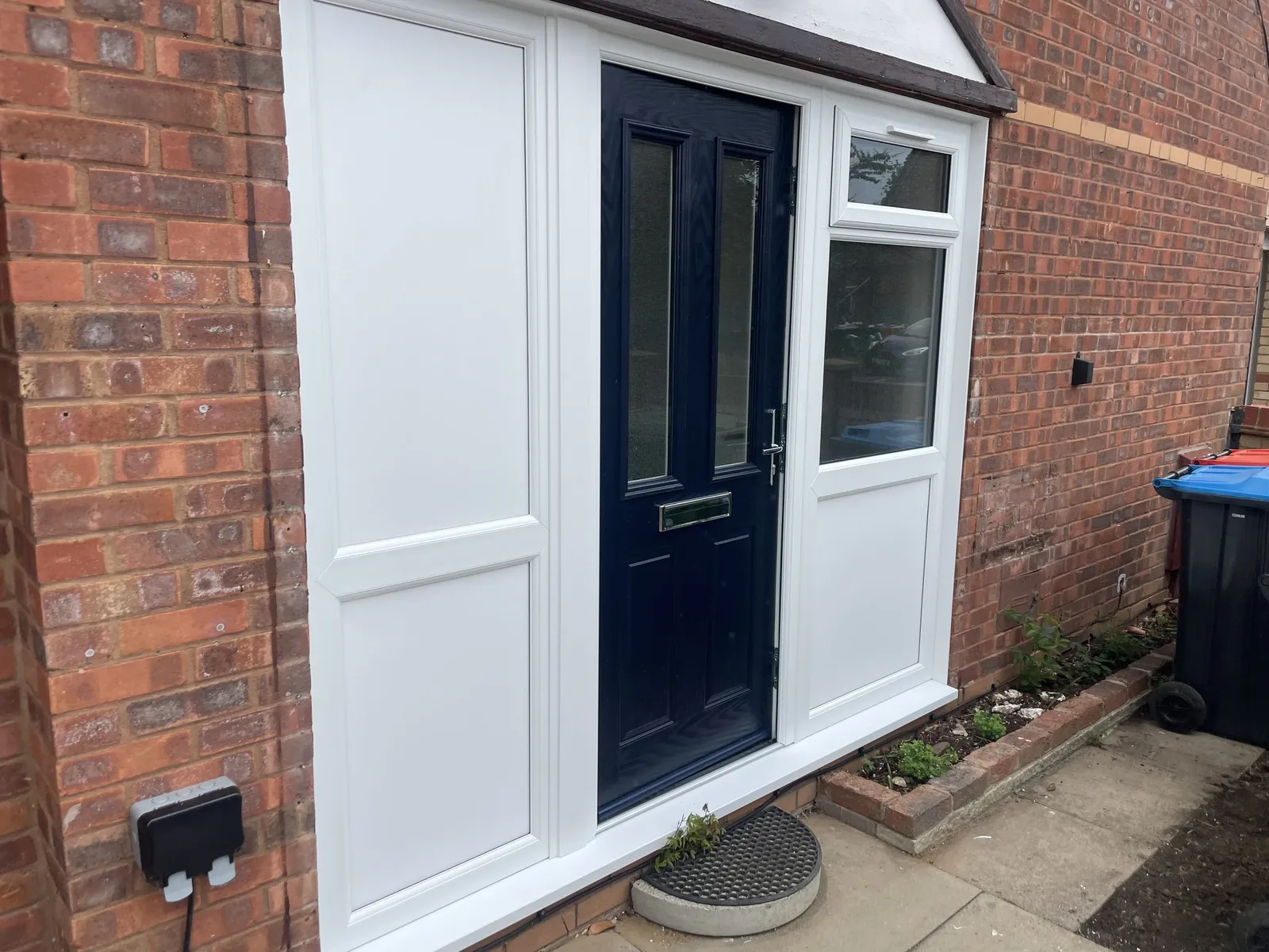Navy blue composite door set into a white uPVC entrance screen with a solid side panel and a glazed window above a panel.