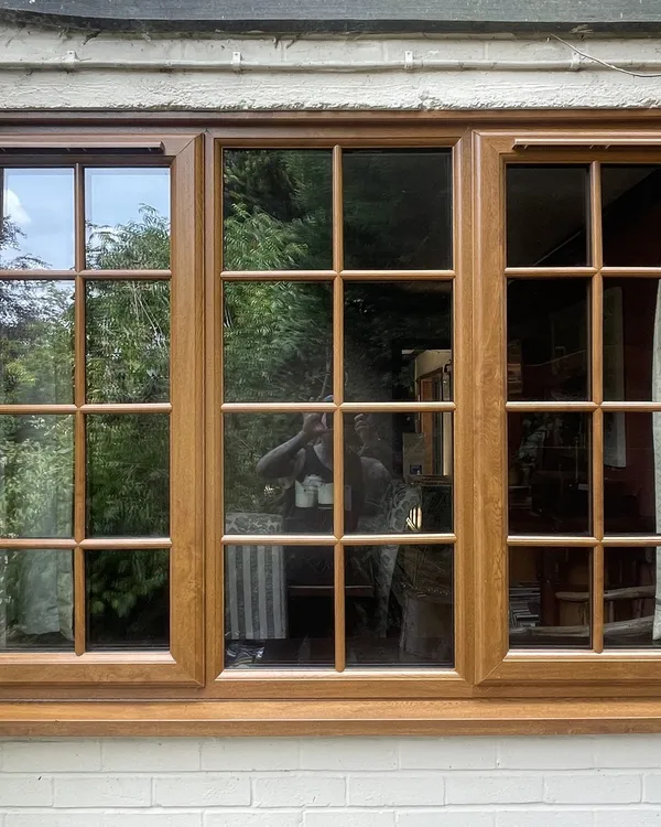 Three-pane golden oak woodgrain uPVC window with Georgian bars, fitted in a white painted brick wall.