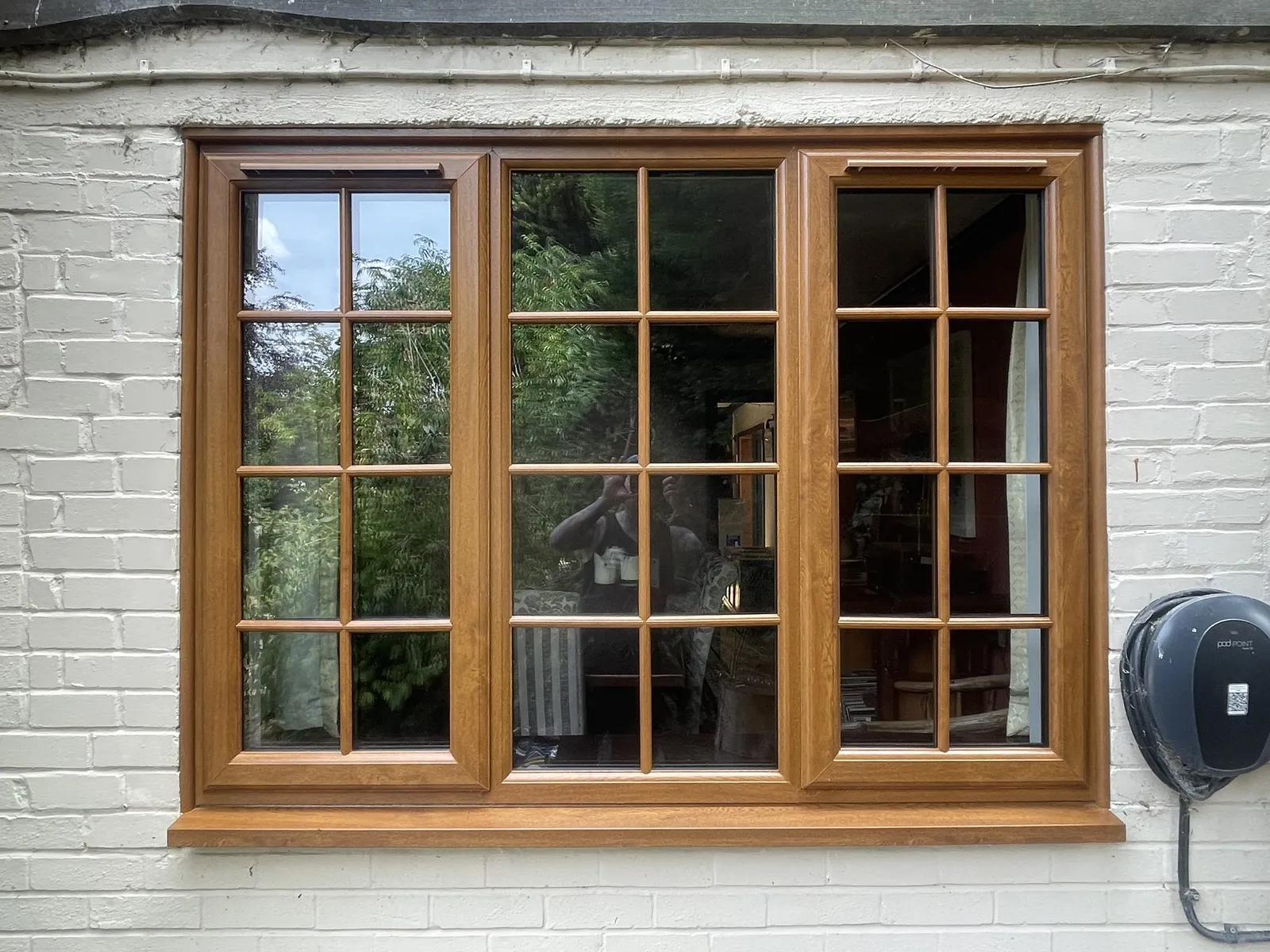 Three-pane golden oak woodgrain uPVC window with Georgian bars, fitted in a white painted brick wall.