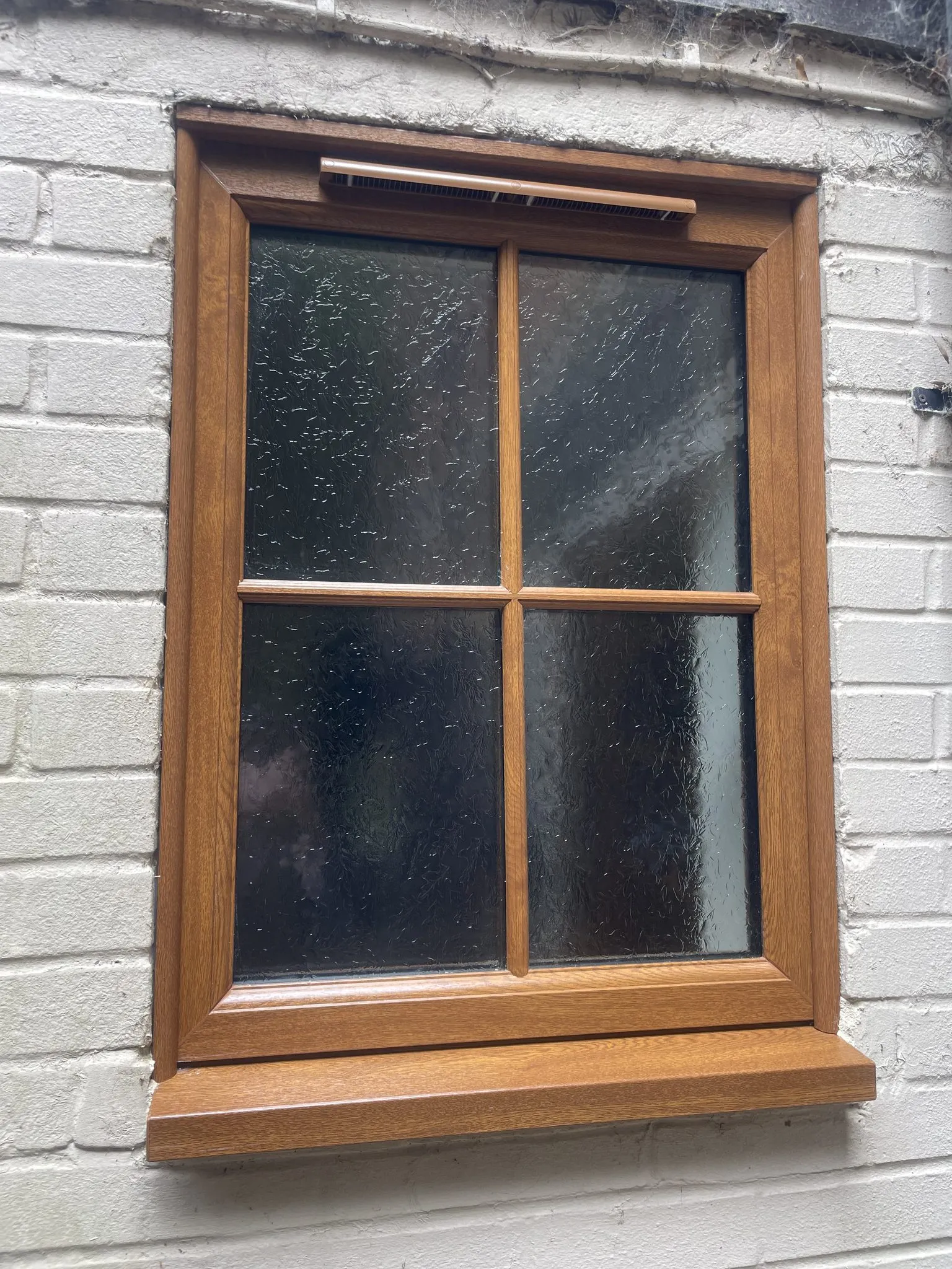 Golden oak woodgrain uPVC window with Georgian bars and obscure glass, fitted in a painted brick wall.