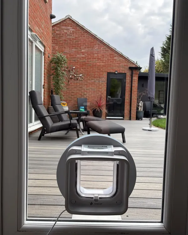 Grey OnlyCat pet door with a display screen fitted into the glazed panel of a patio door overlooking a decked garden.
