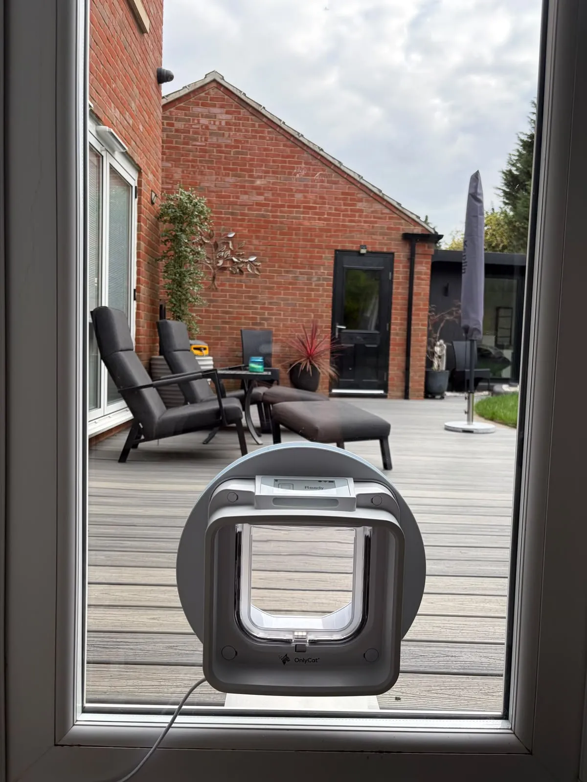 Grey OnlyCat pet door with a display screen fitted into the glazed panel of a patio door overlooking a decked garden.