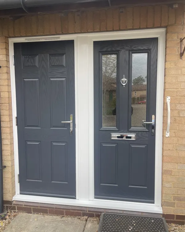 Two anthracite grey composite doors side by side in a shared white frame, one with glazed panels and one solid panelled.