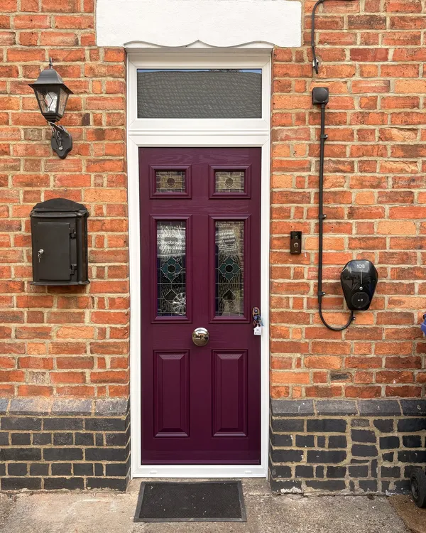 Plum composite front door with stained glass panels, a glazed toplight above and a white frame, on a Victorian red brick terrace.