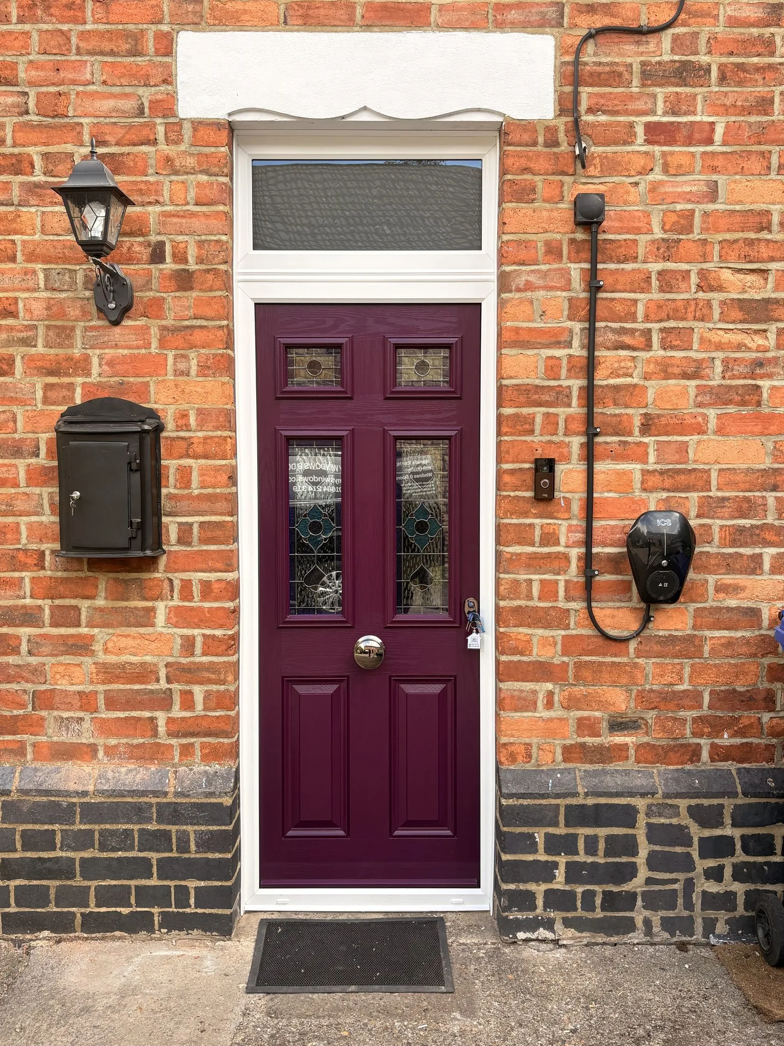 Plum composite front door with stained glass panels, a glazed toplight above and a white frame, on a Victorian red brick terrace.
