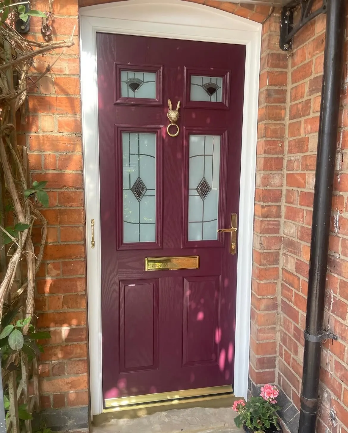 Purple composite front door with decorative glass panels, brass furniture and a brass hare knocker, in a white frame.