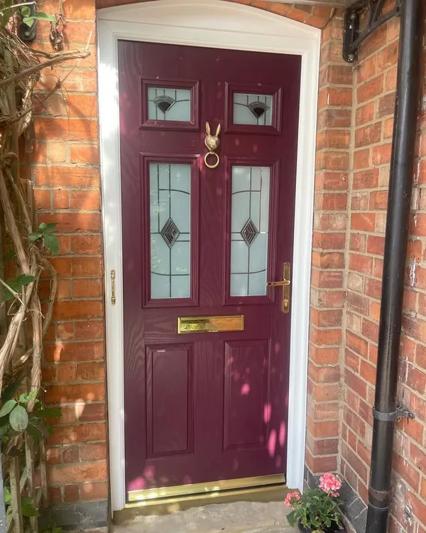 Purple composite front door with decorative glass panels, brass furniture and a brass hare knocker, in a white frame.