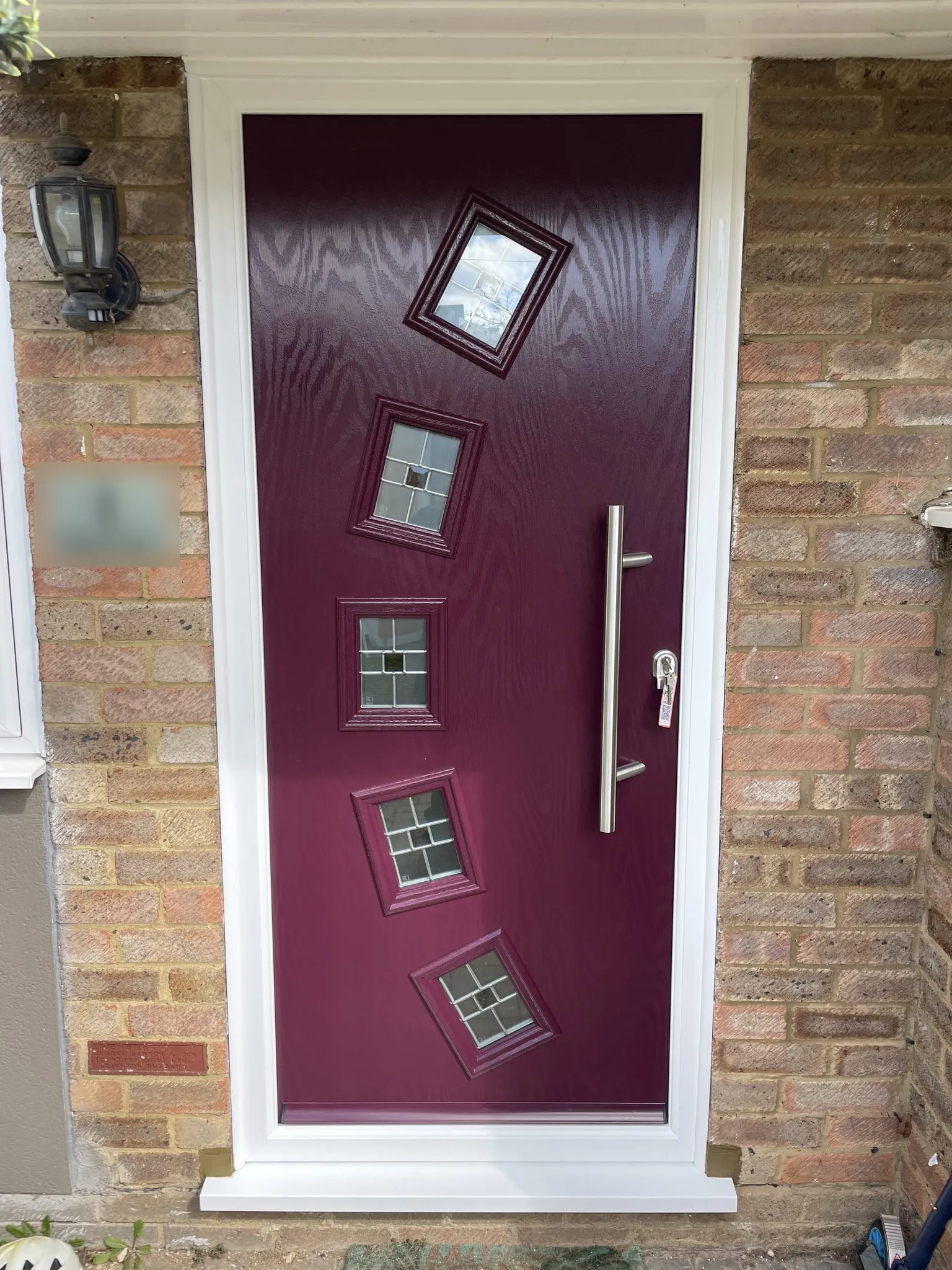 Contemporary purple composite front door with five small tilted square glass panels and a long stainless steel bar handle, in a white frame.