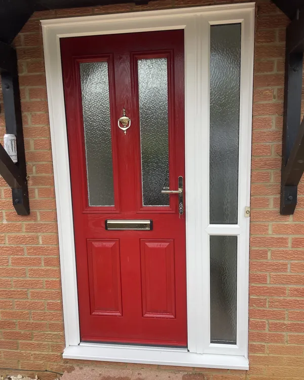 Red composite front door with obscure glass panels and chrome furniture, in a white frame with a glazed side panel beneath a timber canopy.