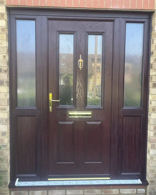 Rosewood-effect composite front door with two glazed panels and brass furniture, flanked by matching side panels with obscure glass.