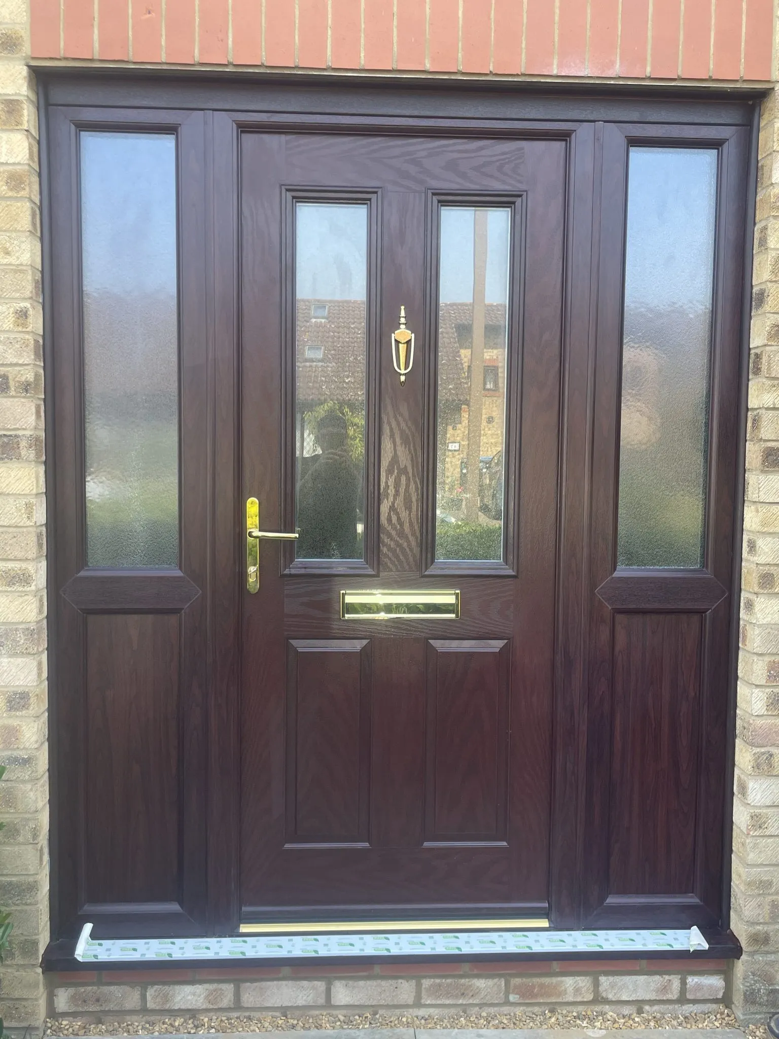 Rosewood-effect composite front door with two glazed panels and brass furniture, flanked by matching side panels with obscure glass.