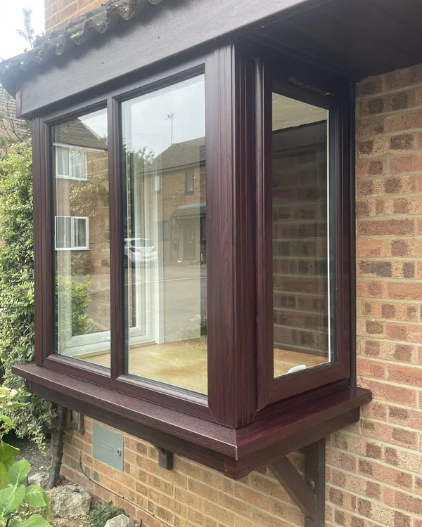 Rosewood-effect uPVC box bay window with clear glazing on a red brick house.
