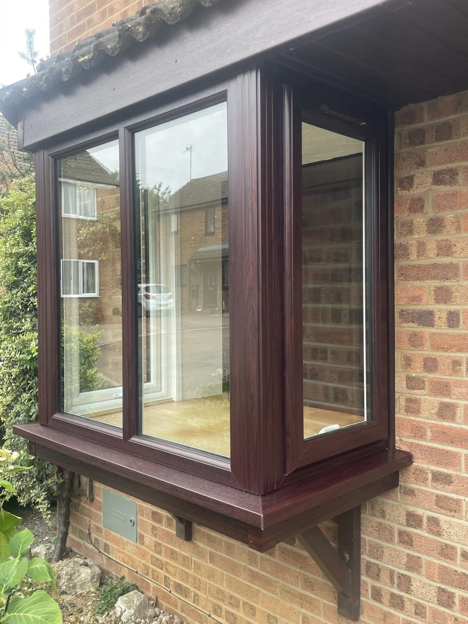 Rosewood-effect uPVC box bay window with clear glazing on a red brick house.