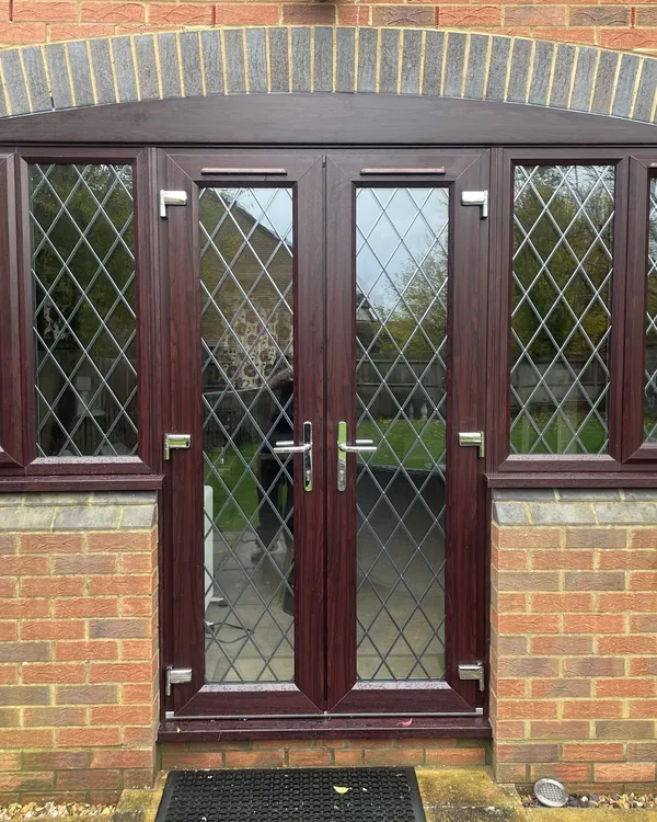 Rosewood-effect uPVC French doors with diamond leaded glass and matching leaded side windows under a brick arch.