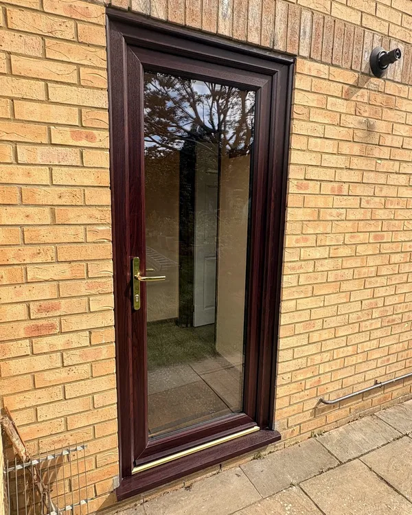 Rosewood-effect uPVC back door with a full-height clear glass panel and brass handle, in a buff brick wall.