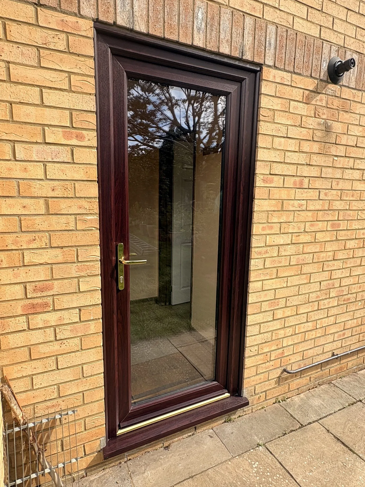 Rosewood-effect uPVC back door with a full-height clear glass panel and brass handle, in a buff brick wall.