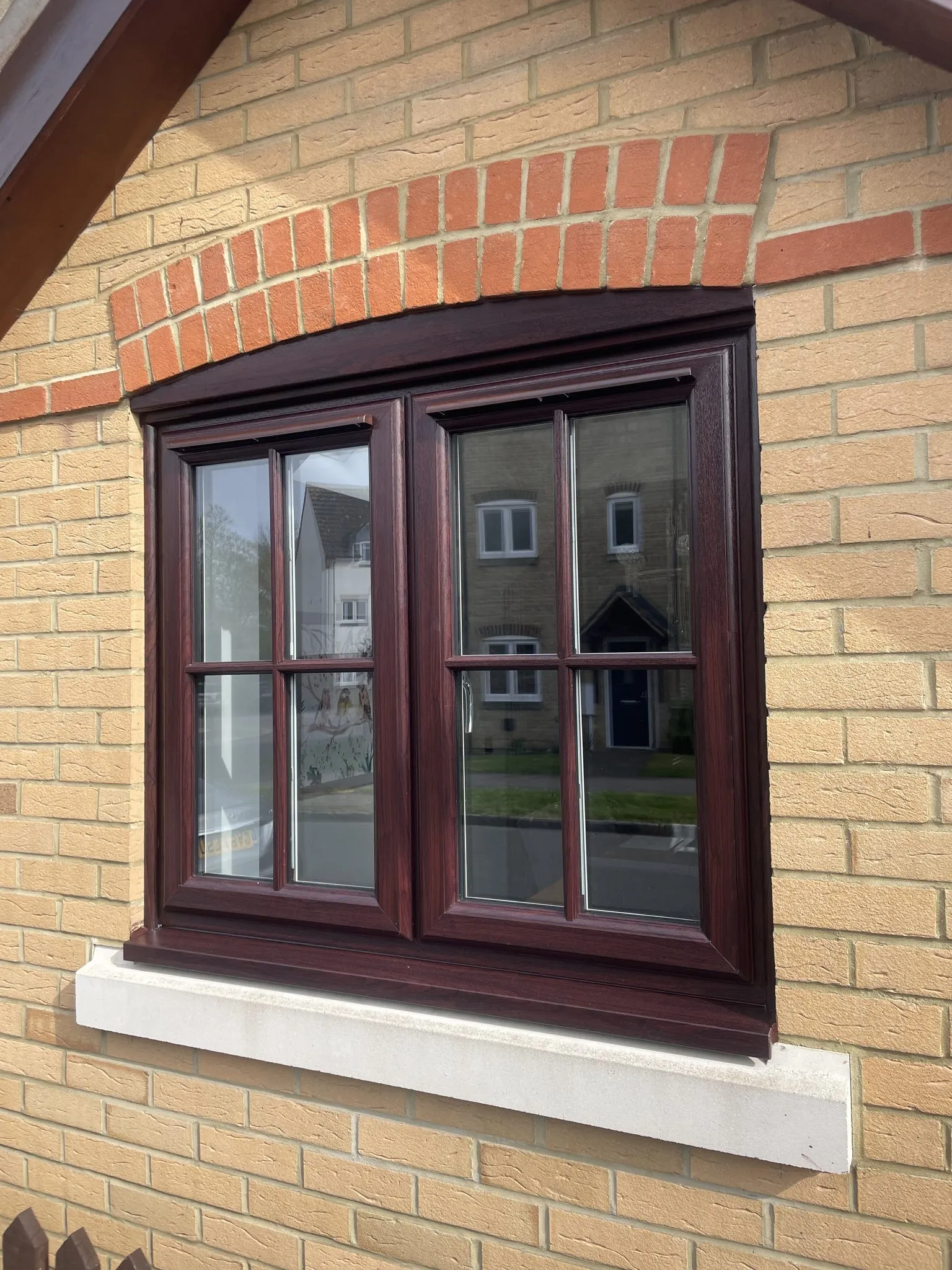 Rosewood-effect uPVC casement window with Georgian bars and a stone sill under a brick arch.
