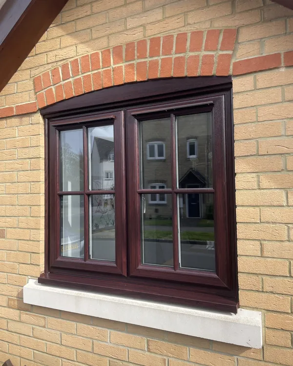 Rosewood-effect uPVC casement window with Georgian bars and a stone sill under a brick arch.