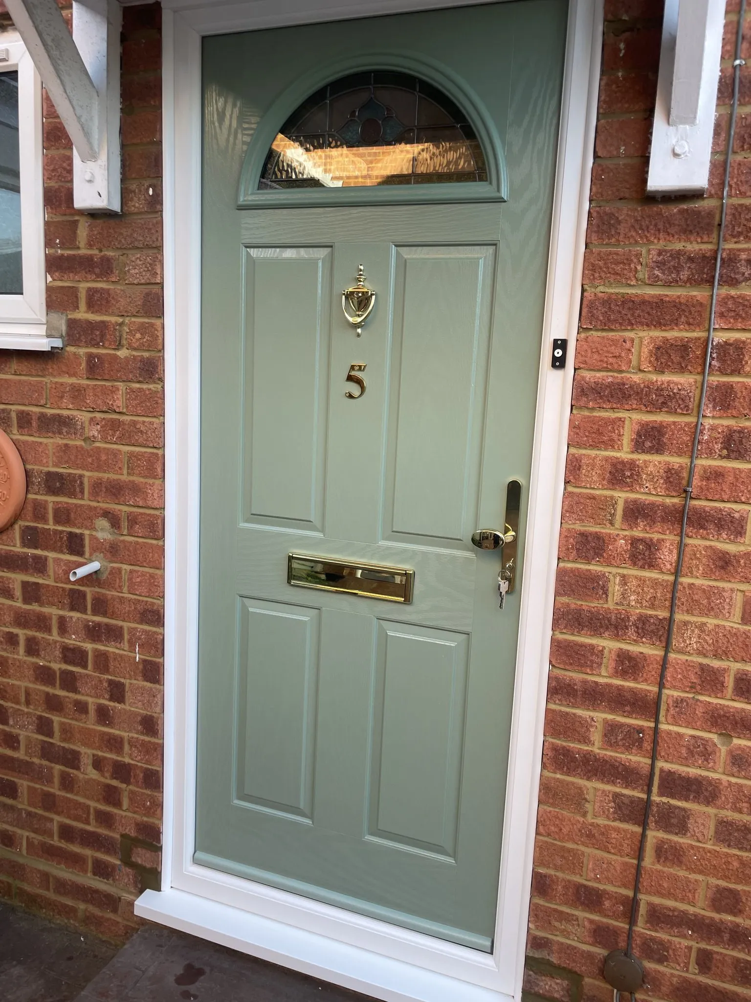 Sage green composite front door with a half-moon decorative glass panel and brass knocker, numeral, handle and letterplate.
