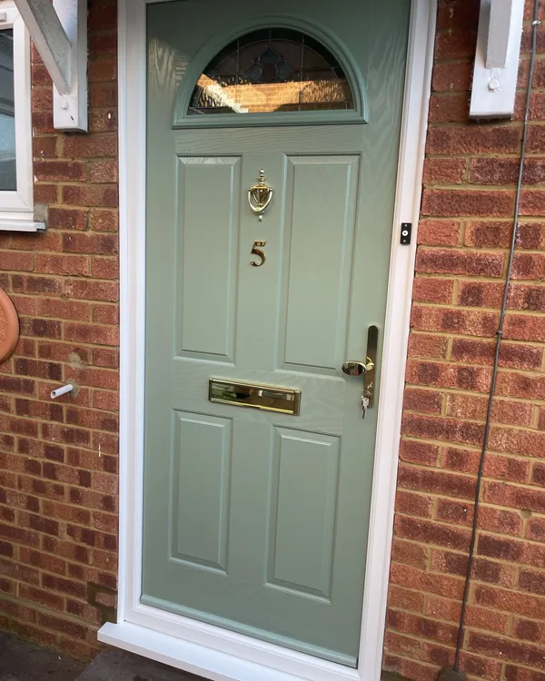 Sage green composite front door with a half-moon decorative glass panel and brass knocker, numeral, handle and letterplate.