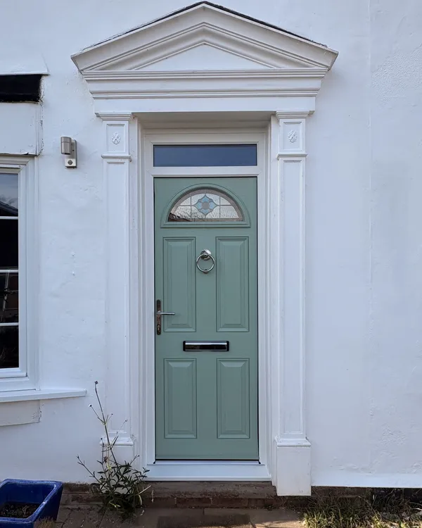 Sage green composite front door with a half-moon glass panel and chrome knocker, set beneath a white pediment door surround.