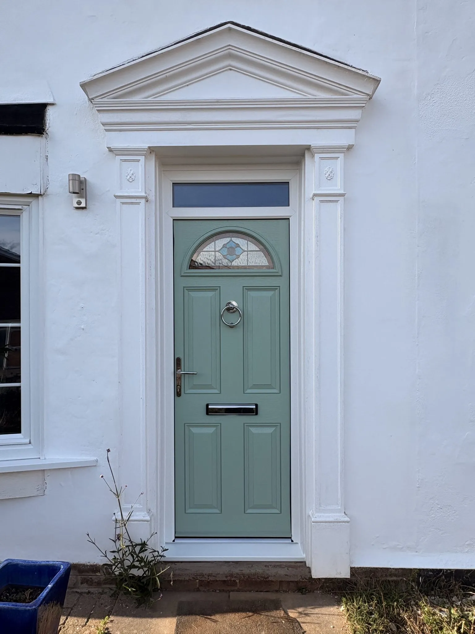 Sage green composite front door with a half-moon glass panel and chrome knocker, set beneath a white pediment door surround.