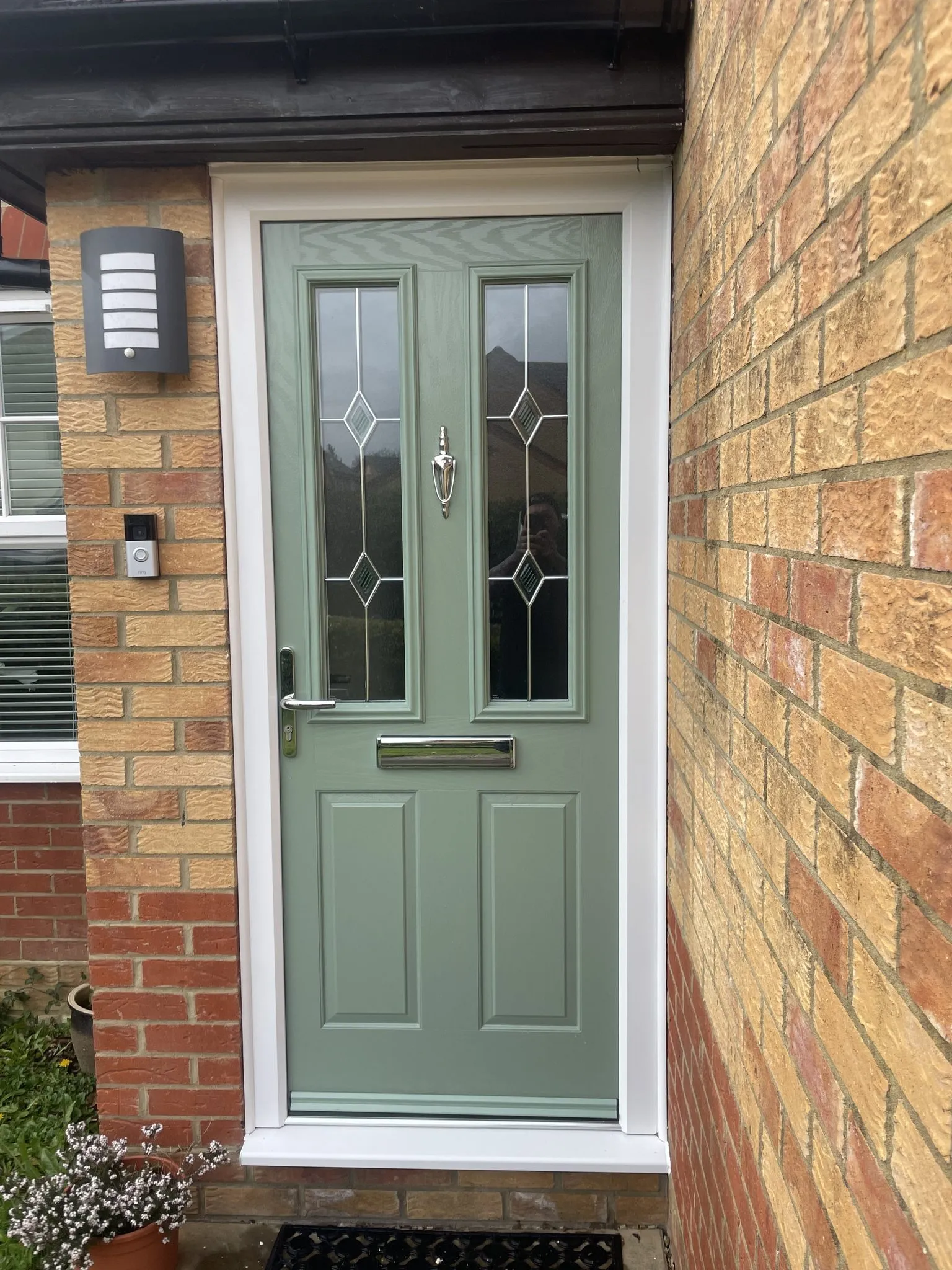 Sage green composite front door with two glazed panels featuring diamond lead detail and a chrome knocker, in a white frame.