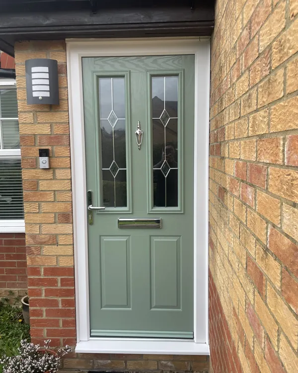Sage green composite front door with two glazed panels featuring diamond lead detail and a chrome knocker, in a white frame.