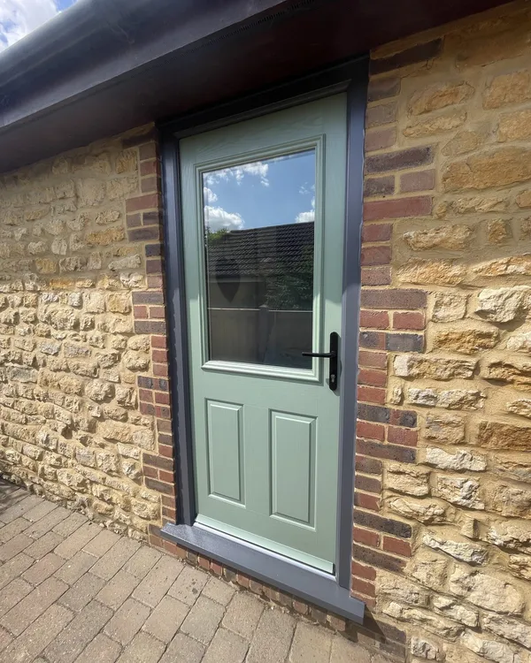 Sage green half-glazed composite door in an anthracite grey frame, set into an ironstone and brick wall.