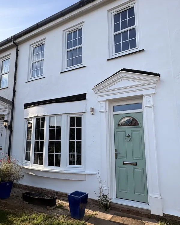 White rendered townhouse with a sage green composite front door beneath a pediment surround and white sash-style windows.
