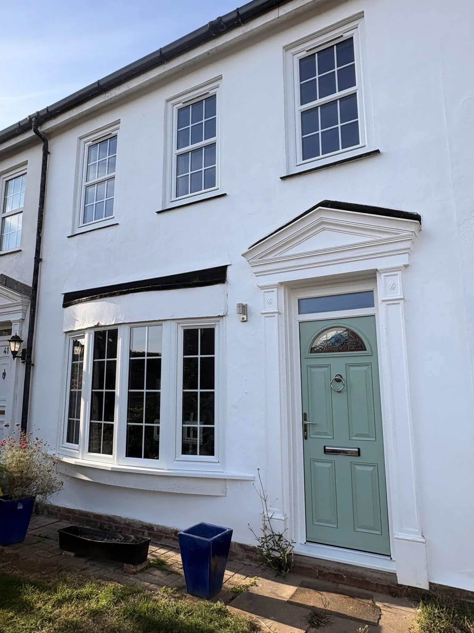 White rendered townhouse with a sage green composite front door beneath a pediment surround and white sash-style windows.