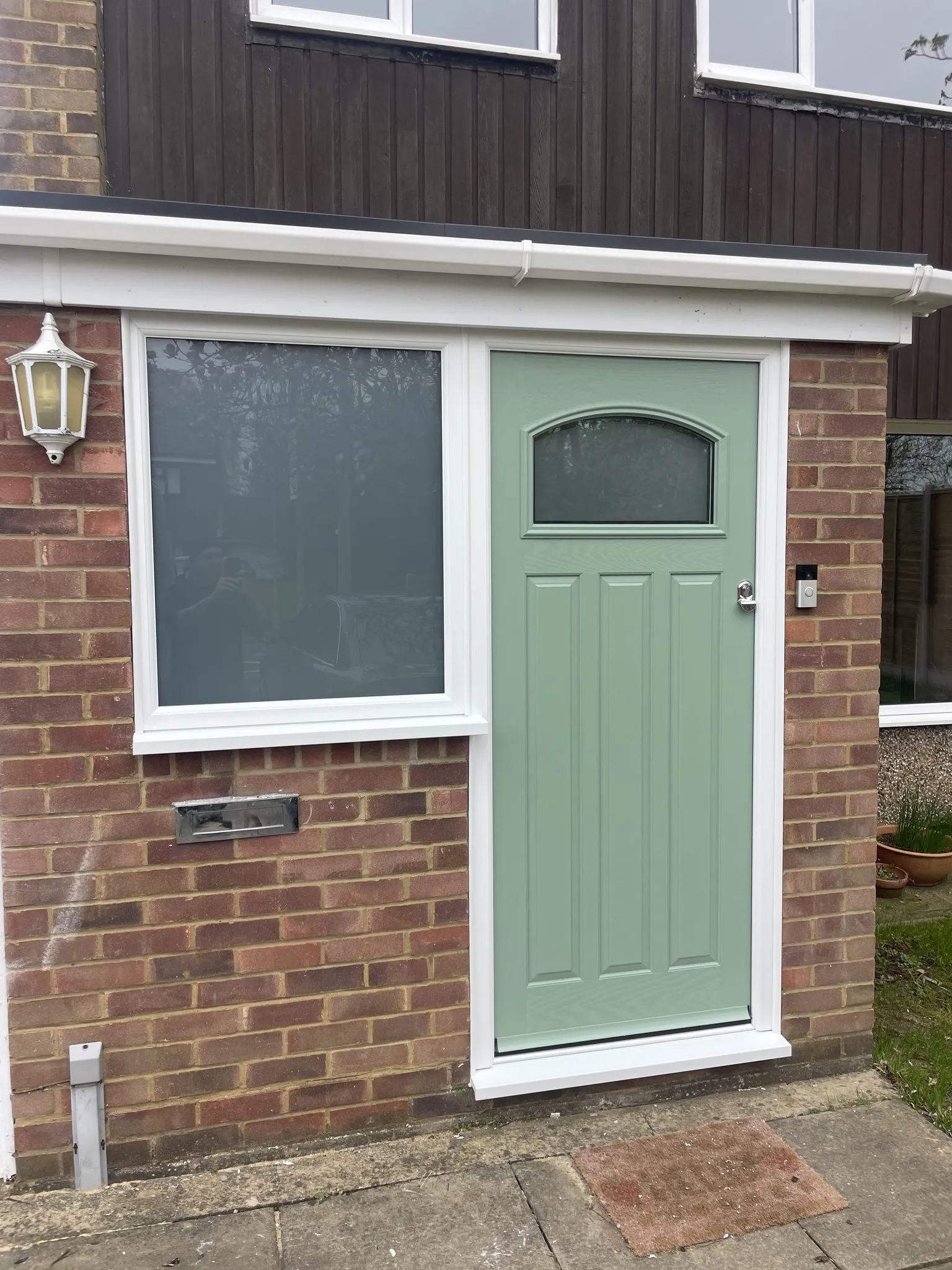 Sage green cottage-style composite door with a small arched glass panel beside a white uPVC window with obscure glass.