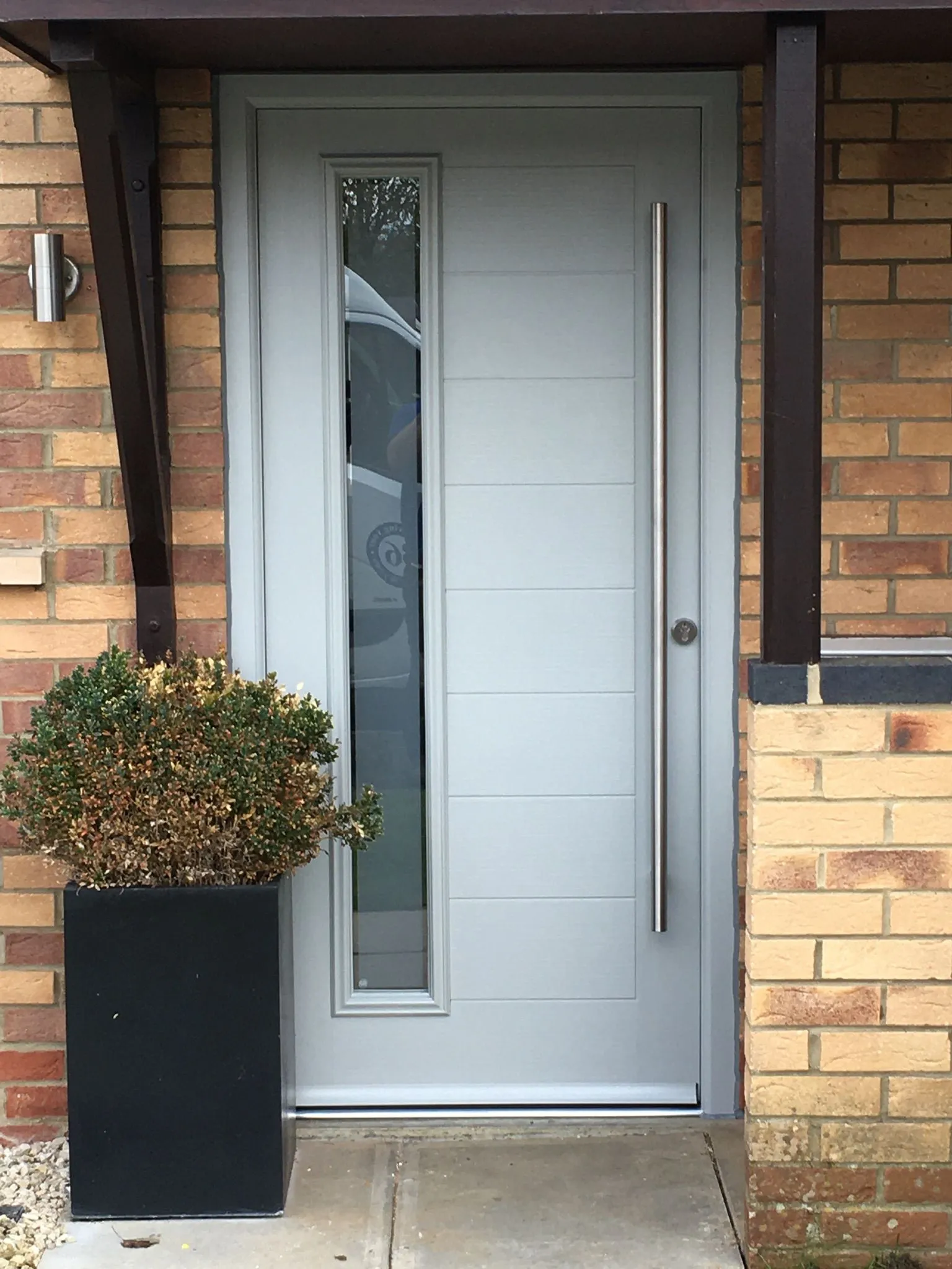 Light grey composite front door with modern handle and glazed side panel