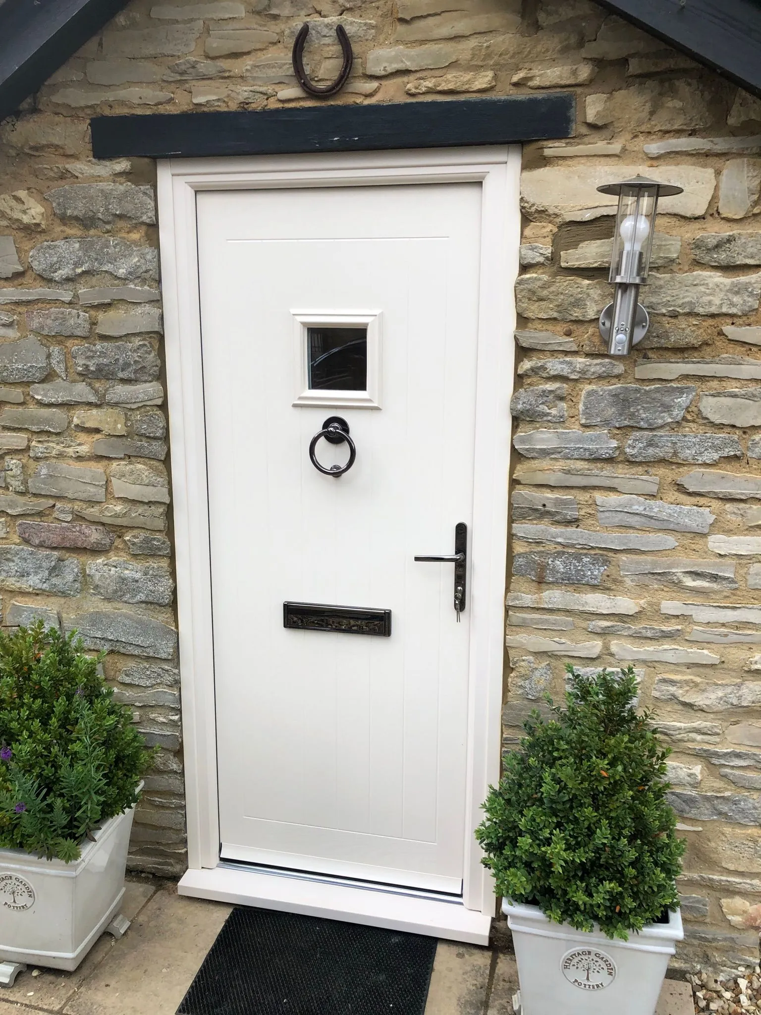White composite front door with square glazed panel in a stone cottage