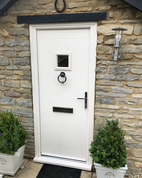 White composite front door with square glazed panel in a stone cottage