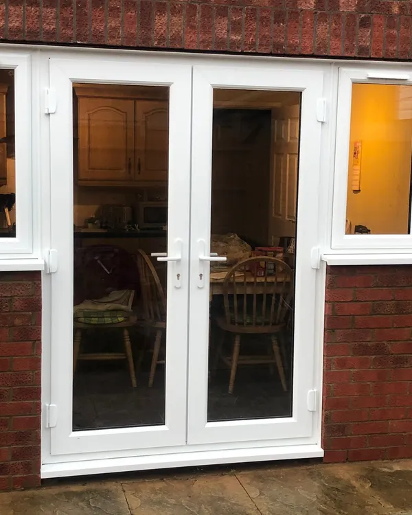 White uPVC French doors with glazed side windows fitted in a brick exterior.