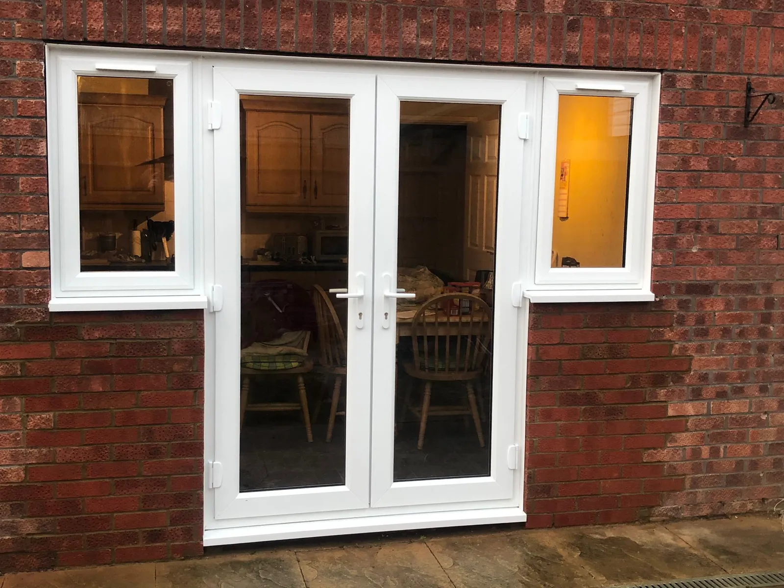 White uPVC French doors with glazed side windows fitted in a brick exterior.