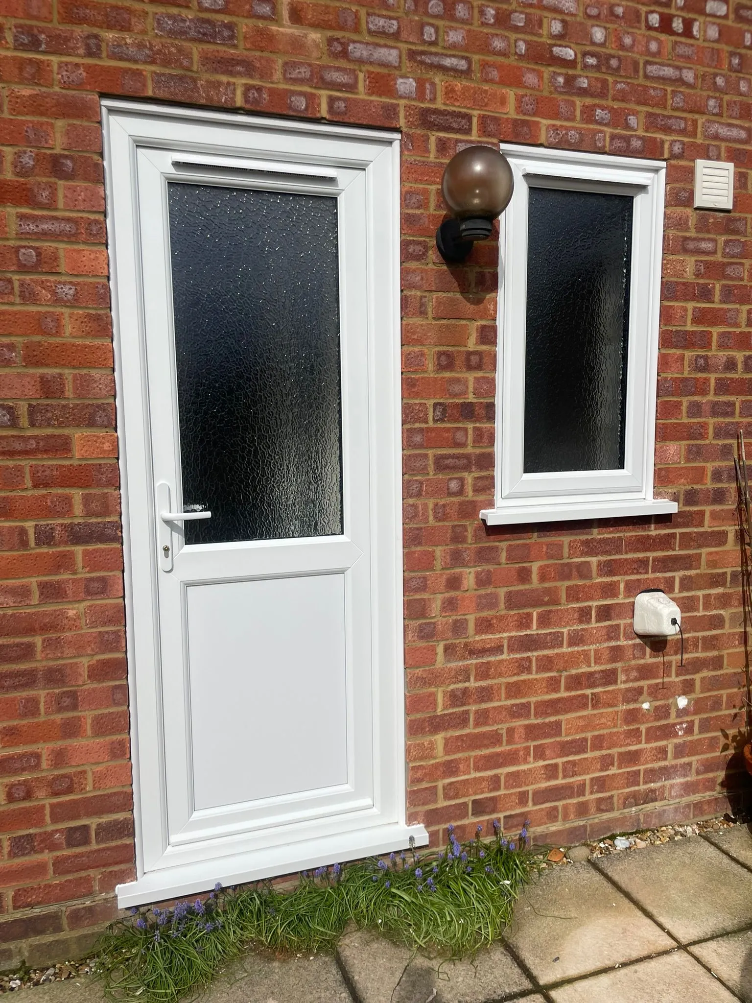White uPVC back door with textured glass and a fixed side window in red brick wall.