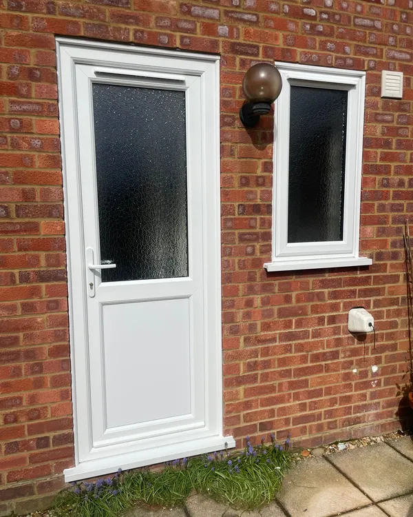 White uPVC back door with textured glass and a fixed side window in red brick wall.