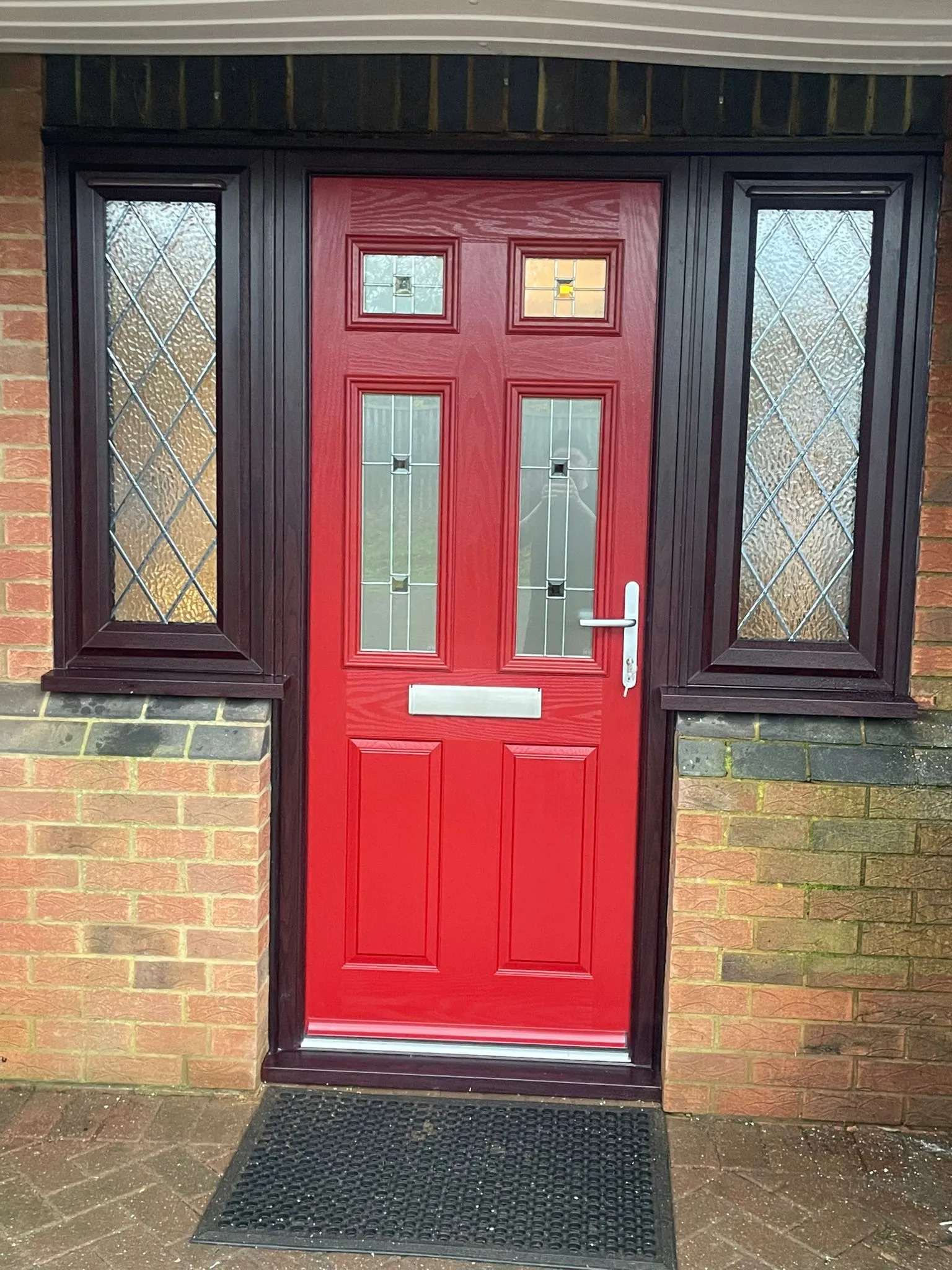 Red composite entrance door with decorative glass and matching side panels.